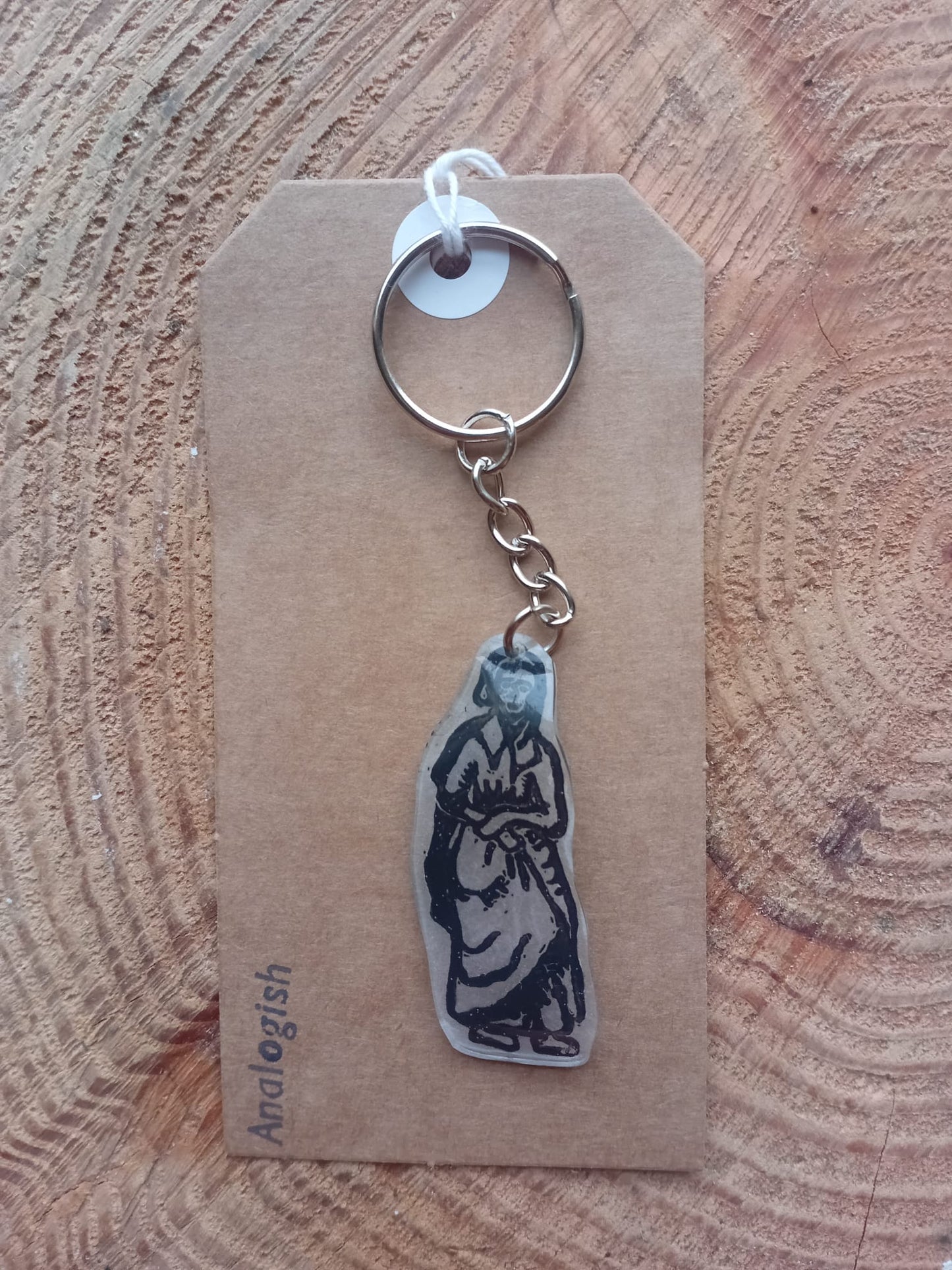 Keychain with a medieval woman design on a brown card with Analogish branding, placed on a wooden surface.