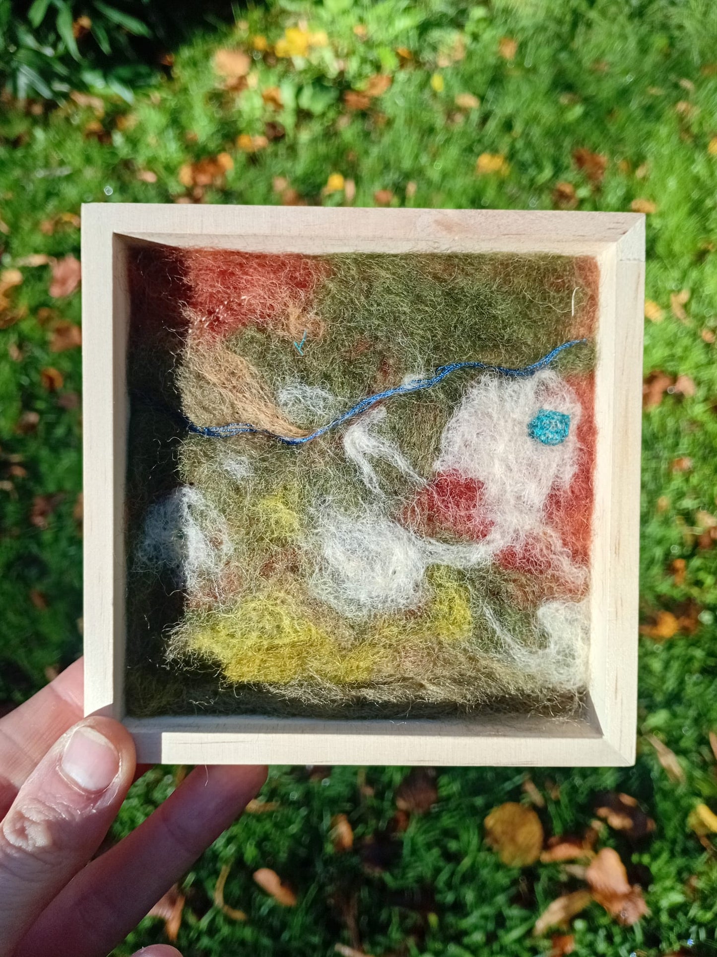Small framed artwork held in front of a grassy background