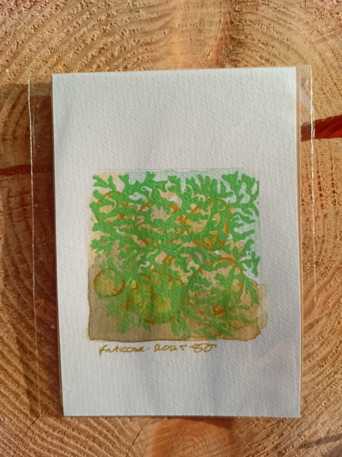 Artistic print of green and brown abstract design on a white card, placed on a wooden surface.