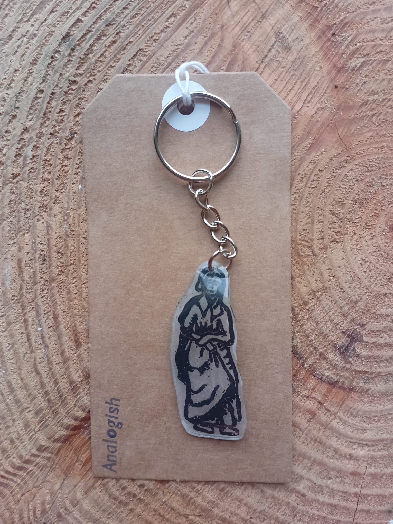 Keychain with a medieval woman design on a brown card with Analogish branding, placed on a wooden surface.