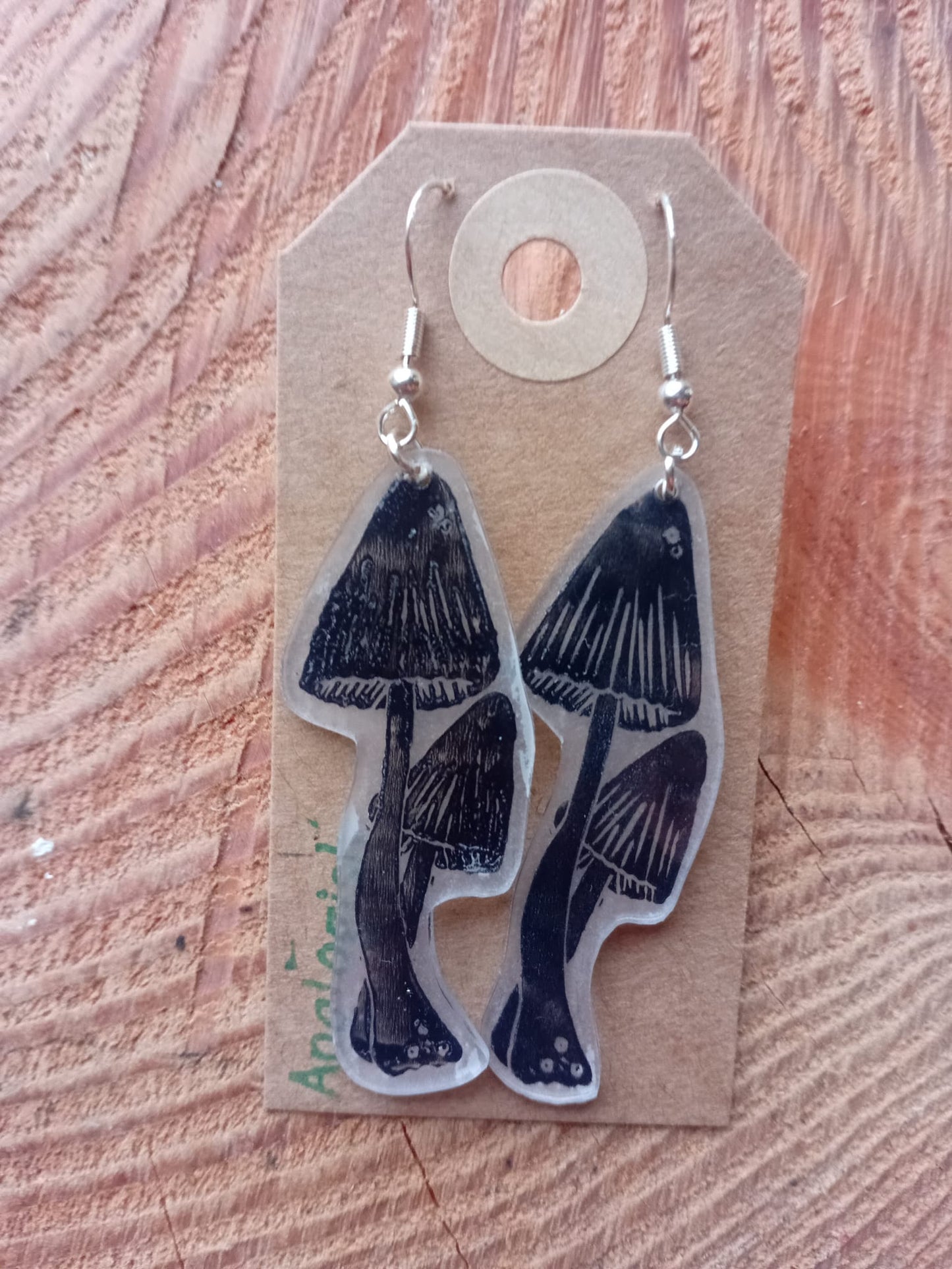 Mushroom-shaped earrings on a cardboard backing with Analogish branding, on a wooden surface.