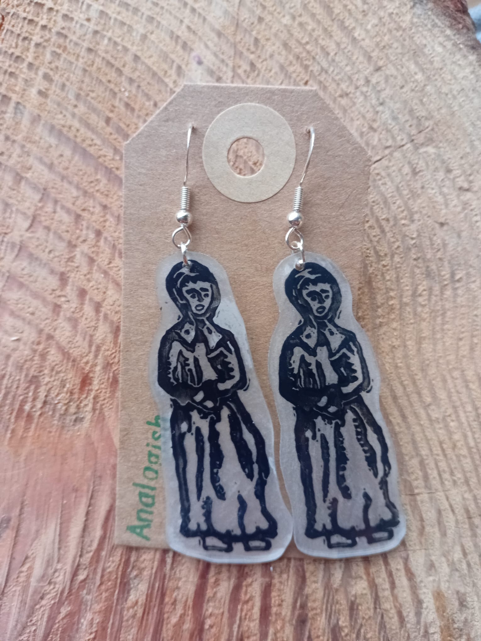 Pair of earrings with a design on a cardboard backing, placed on a wooden surface.