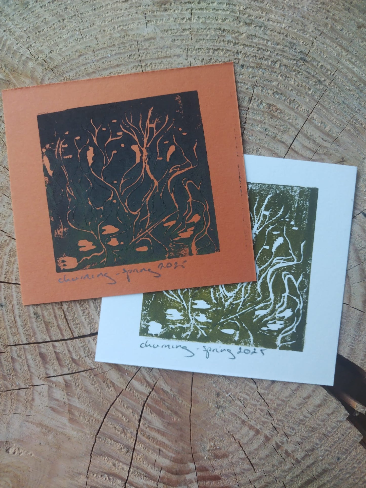 2 prints of Churning, one orange and one white on a wooden background
