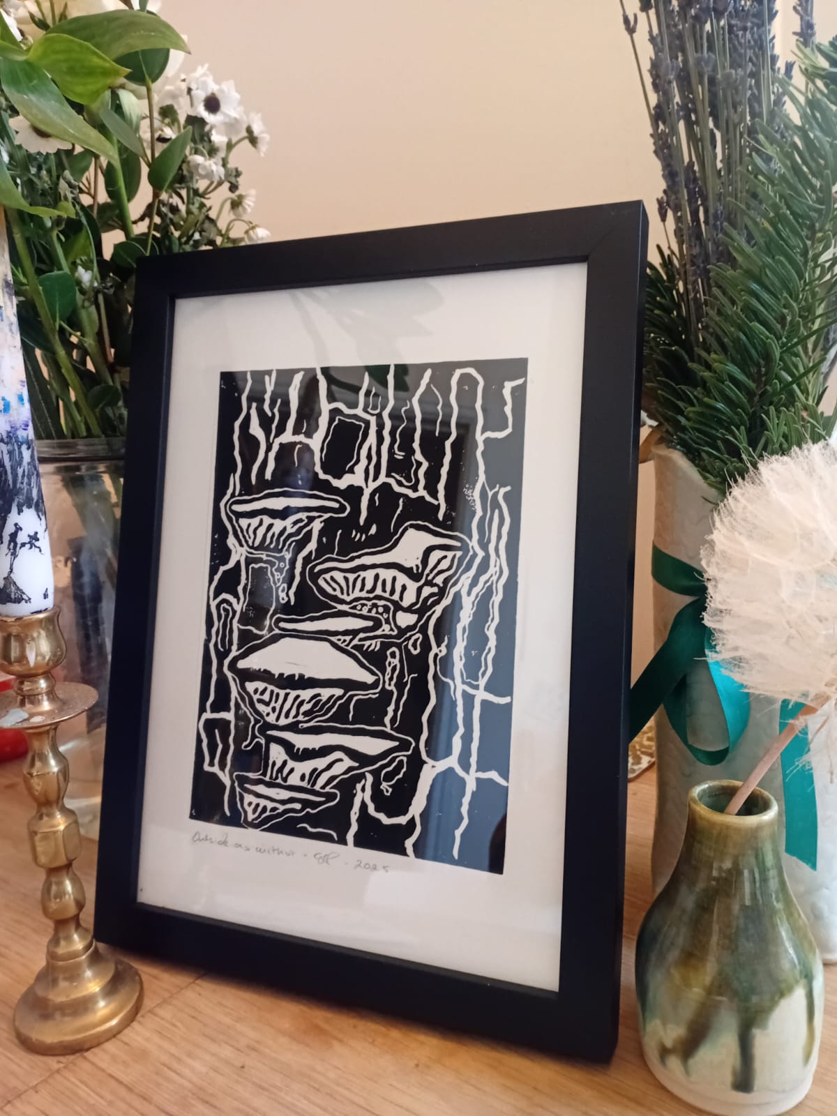 Framed black and white artwork on a table with decorative items. Example of the stand that comes with the artwork.