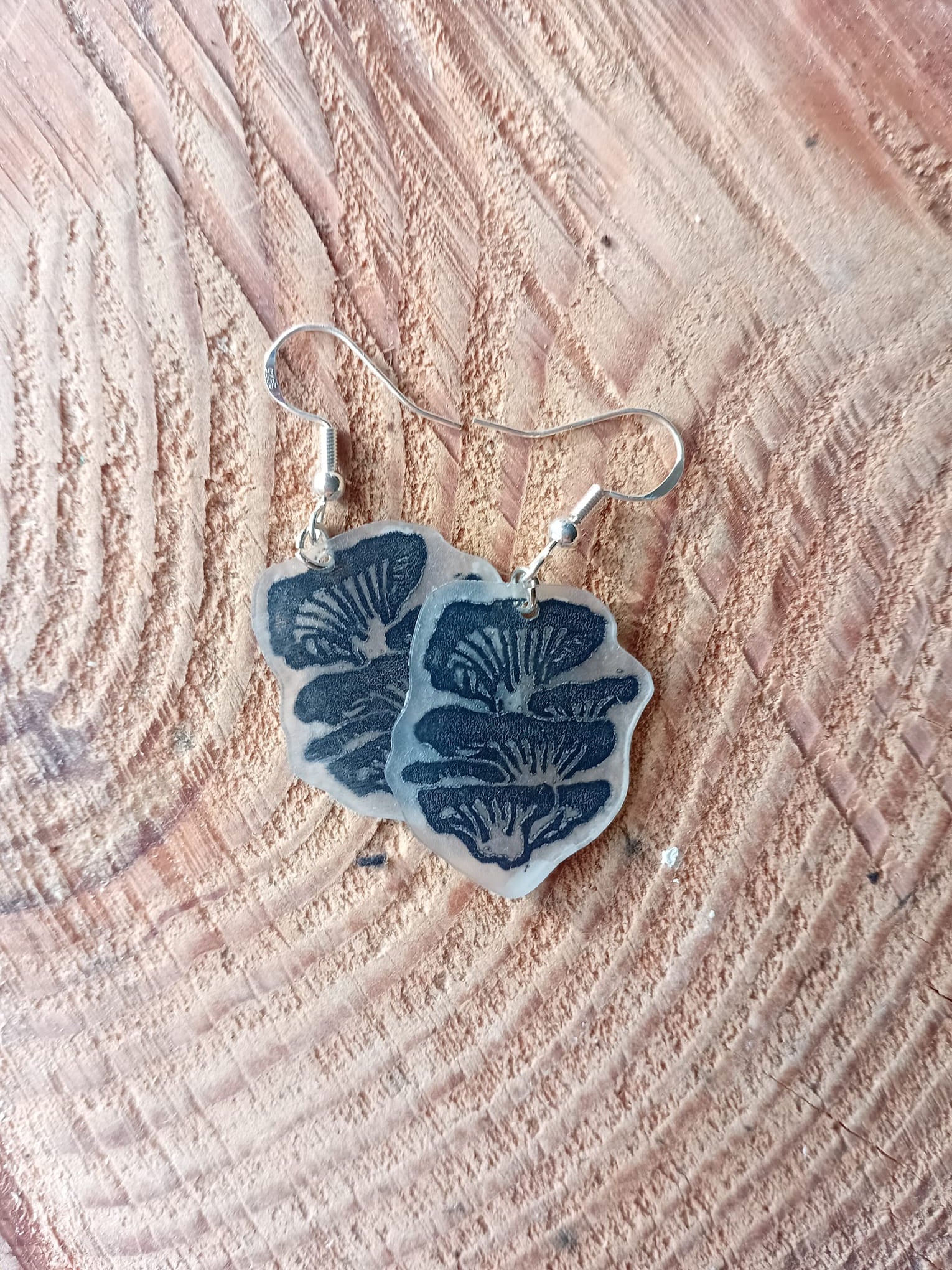 Oyster mushrrom-patterned earrings on a wooden surface