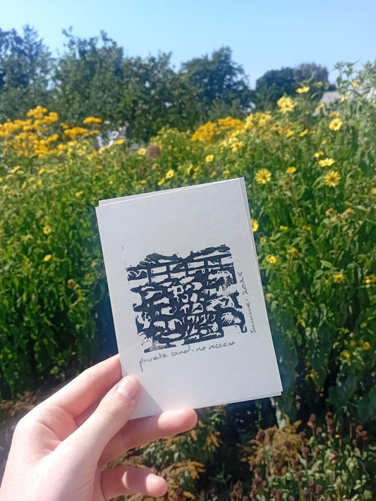Hand holding a white card with black text against a background of yellow flowers and green trees