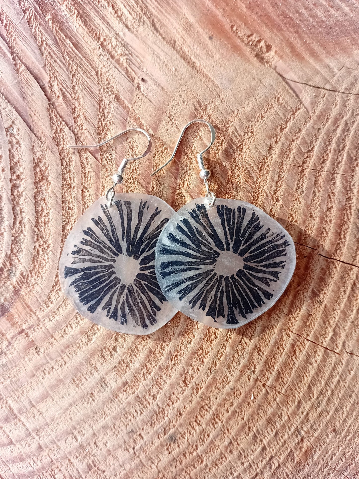 Mushroom-patterned earrings on a textured wooden surface