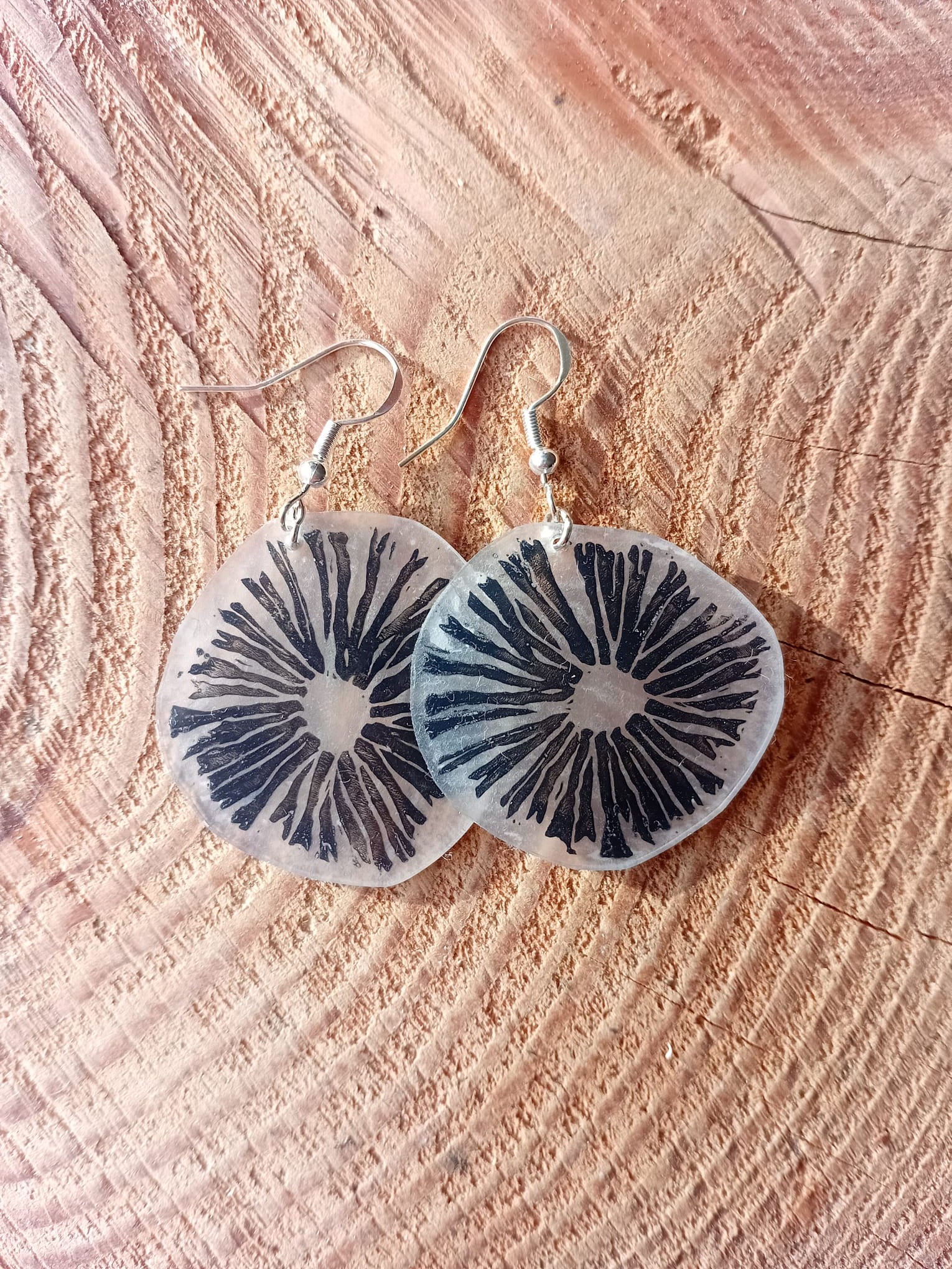 Mushroom-patterned earrings on a textured wooden surface