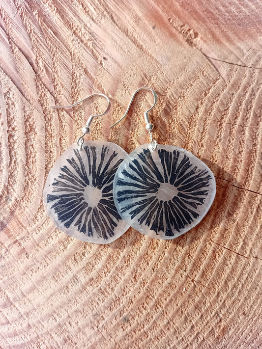 Mushroom-patterned earrings on a textured wooden surface
