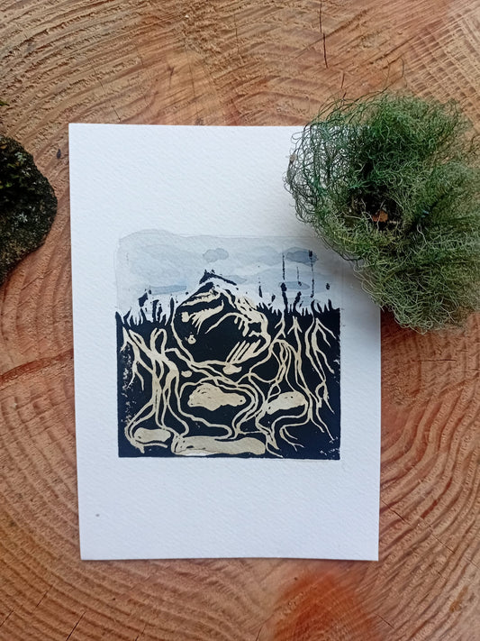 Woodcut-style lino print of rocks and bones on a white card with a watercolour background